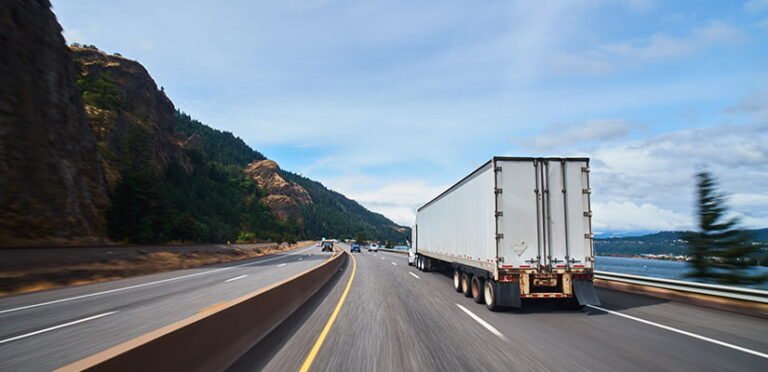 A white semi truck on a highway beside a river and hills.