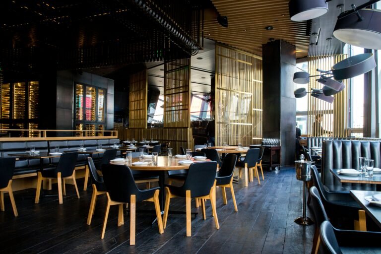 An empty modern restaurant dining room with dark wood walls and set tables.