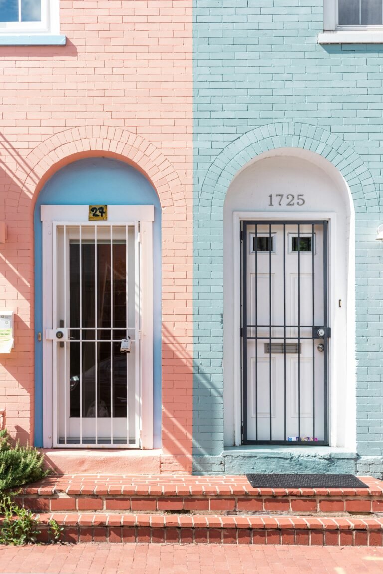 Two narrow row-house fronts, one pink and one light blue, each with an arched white door.