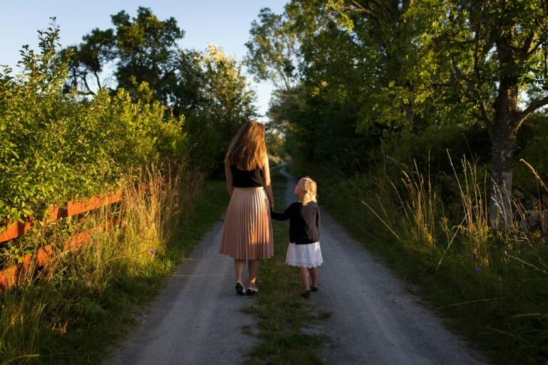 A parent and a young child walking hand in hand down a tree-lined country path.